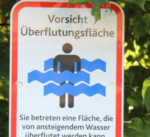 Warnschild für eine Überflutungsfläche vor einem Busch