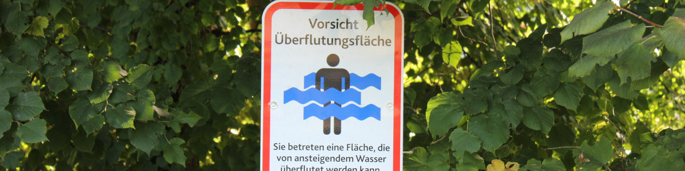 Warnschild für eine Überflutungsfläche vor einem Busch